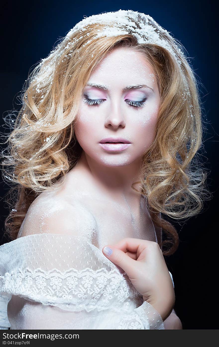 The beautiful blond girl with a winter make-up in a white attire on a dark blue background