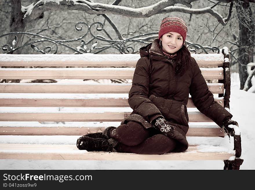 Young woman in a red cap in winter park on a bench. Young woman in a red cap in winter park on a bench