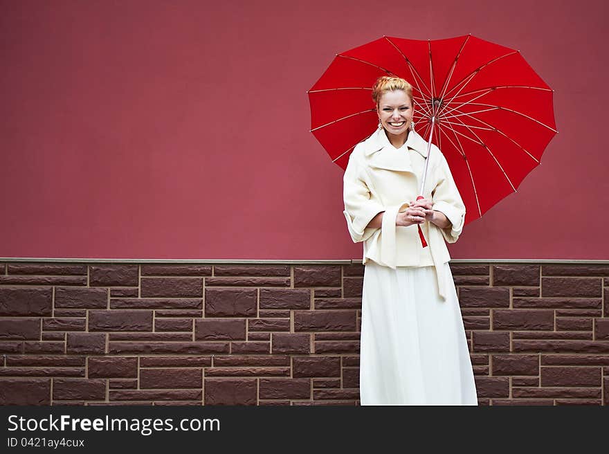 Woman in white coat with red umbrella near burgundy walls