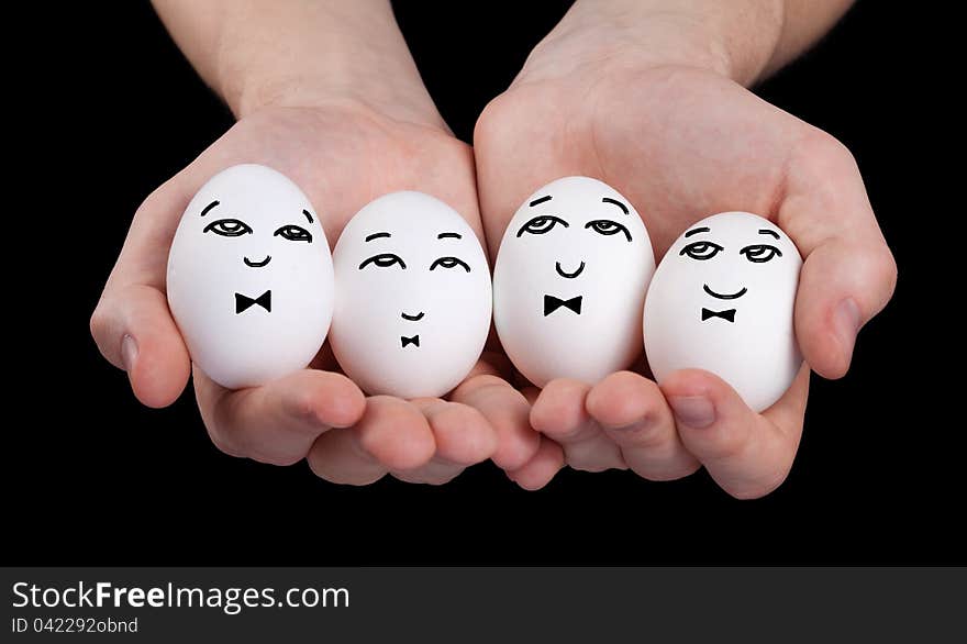 Hand holding cute eggs with funny face smileys on black background