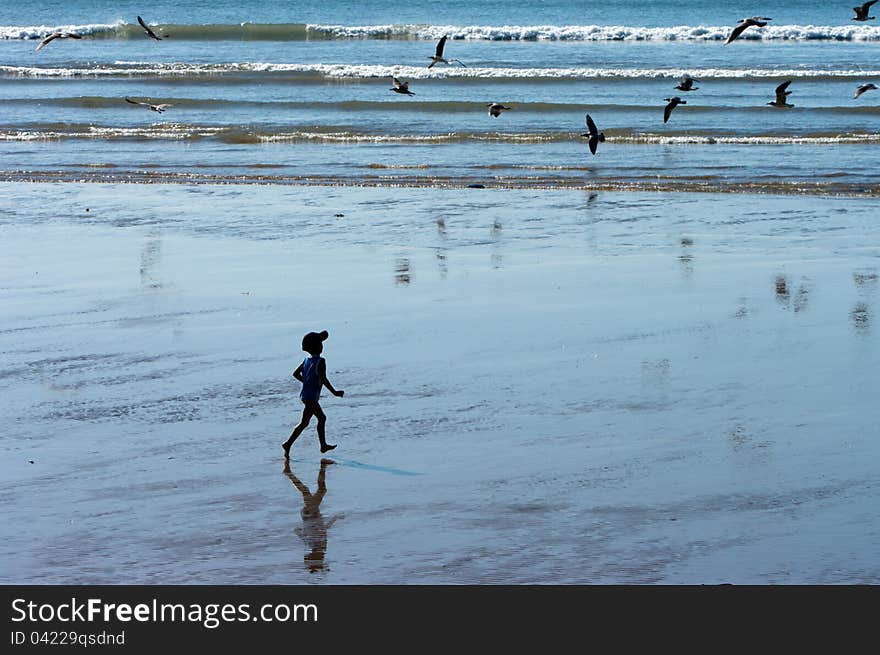 A silhouette of a boy running on the beach towards waves and birds. A silhouette of a boy running on the beach towards waves and birds