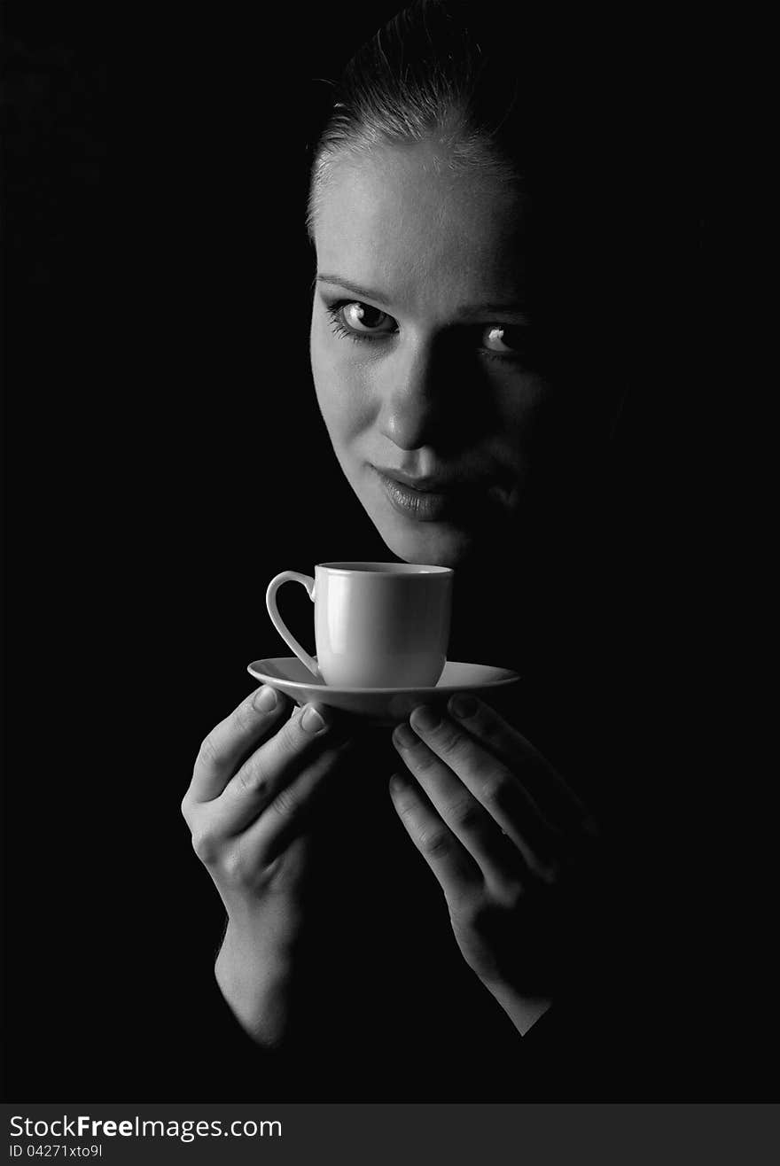 Monochrome portrait of a beautiful girl with a cup of coffee on a black background. Monochrome portrait of a beautiful girl with a cup of coffee on a black background