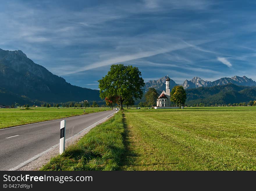 Autumn landscape with road, tree, church, mountains and sky on backgruond