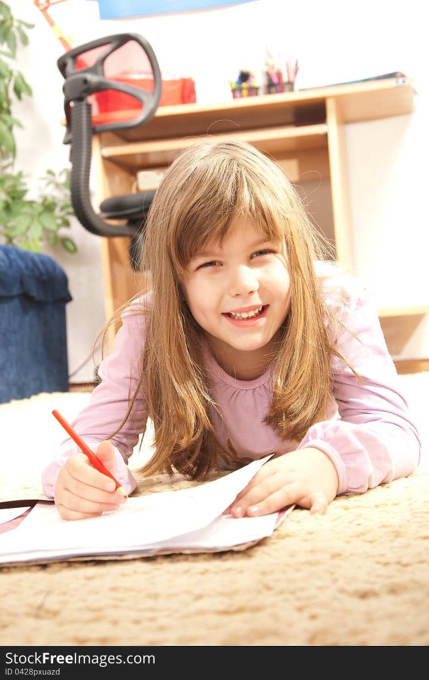 Happy little girl lying on the floor in her room writes. Happy little girl lying on the floor in her room writes