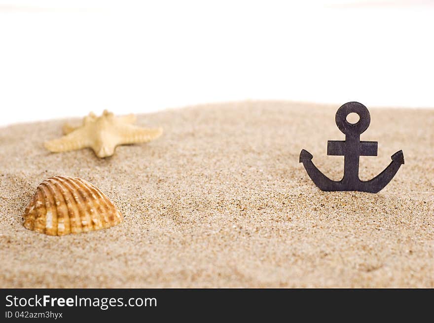 Toylike anchor and seashells on sand isoalted on white background