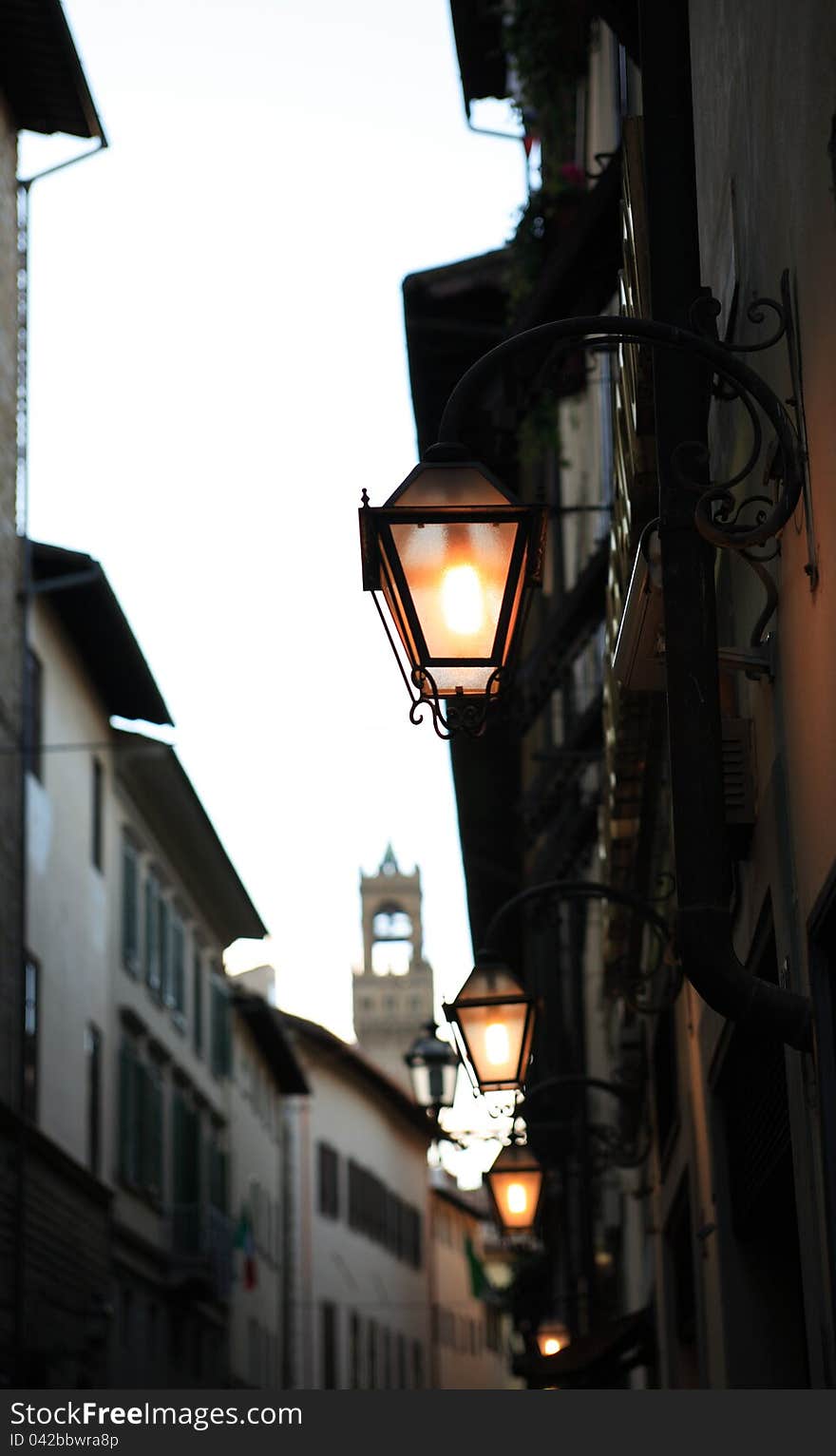 Evening street in Florence. Few glowing vintage street lamps on background with buildings and tower