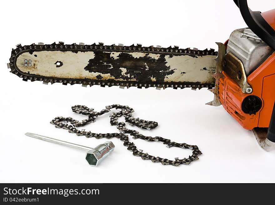 A chain saw with a replacement chain and a tool for installation on a white background into. A chain saw with a replacement chain and a tool for installation on a white background into.