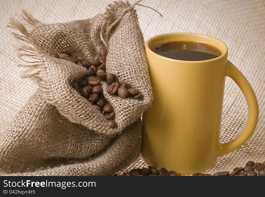 Cup of coffee with beans and sack over brown burlap background. Cup of coffee with beans and sack over brown burlap background