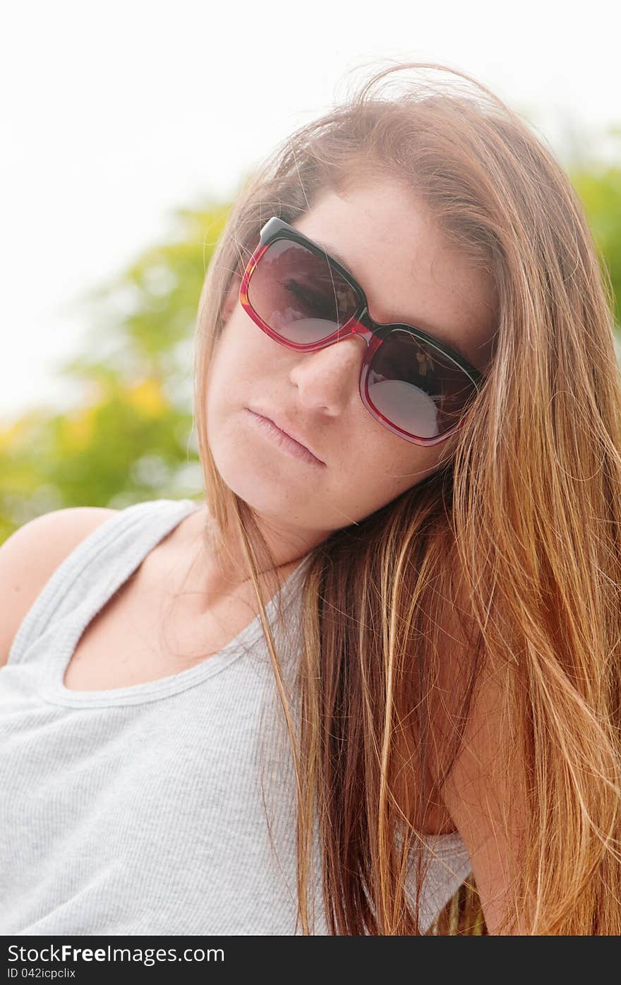 Teen girl outdoors wearing sunglasses, a gray tank top, and long hair. Teen girl outdoors wearing sunglasses, a gray tank top, and long hair