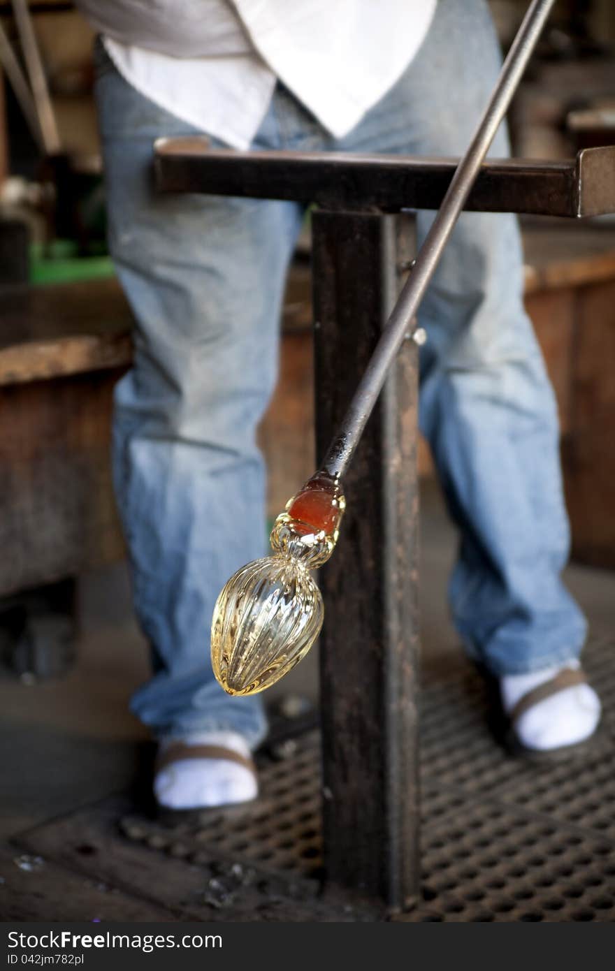 Glass blower shaping molten glass into a drinking goblet using metal tongs