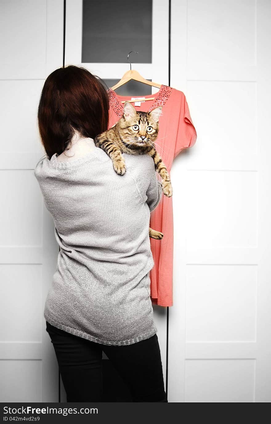 Young woman holding a cat is looking at a dress in front of wardrobe