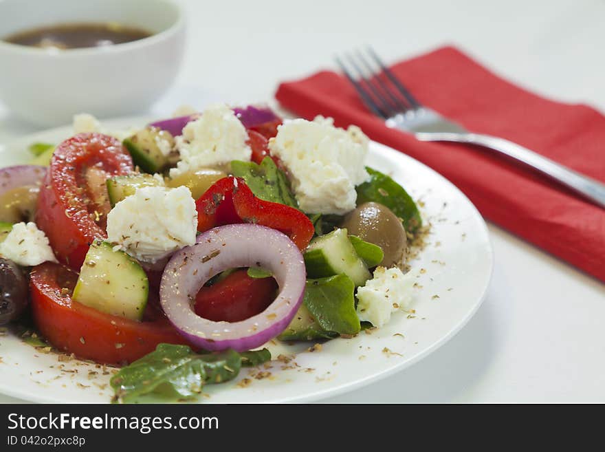 Traditional Greek salad with tomatoes, cucumber, lettuce, olives, peppers and feta cheese served on a white plate