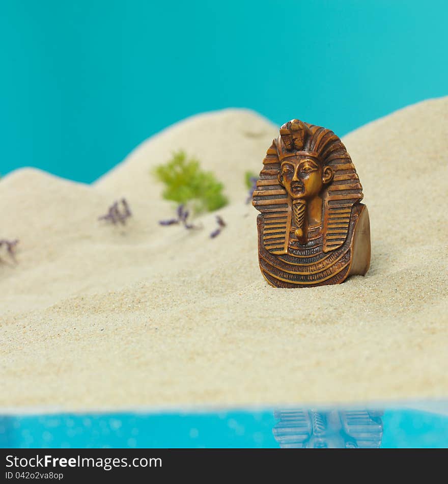 Egyptian tutankhamun bust burried in the sand of a miniature sea shore landscape. Egyptian tutankhamun bust burried in the sand of a miniature sea shore landscape