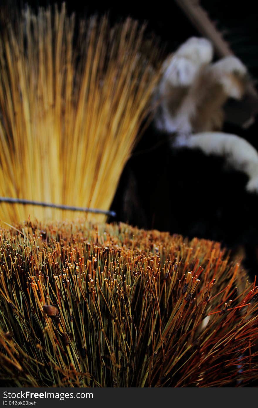 Close up view of bristles of grass broom with other brooms and dusters obscured in background. Close up view of bristles of grass broom with other brooms and dusters obscured in background