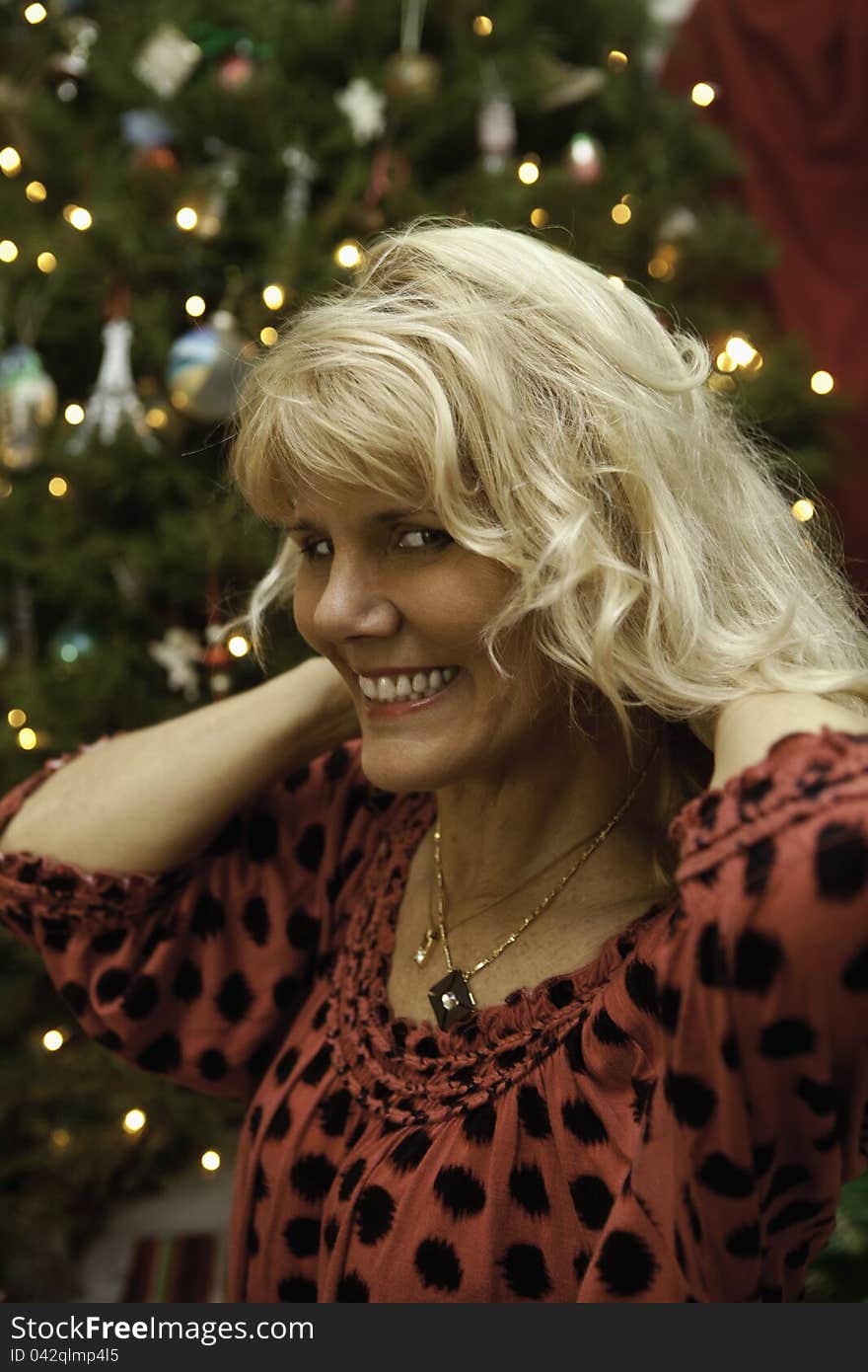 Middle age woman at christmas putting on a necklace in front of the tree