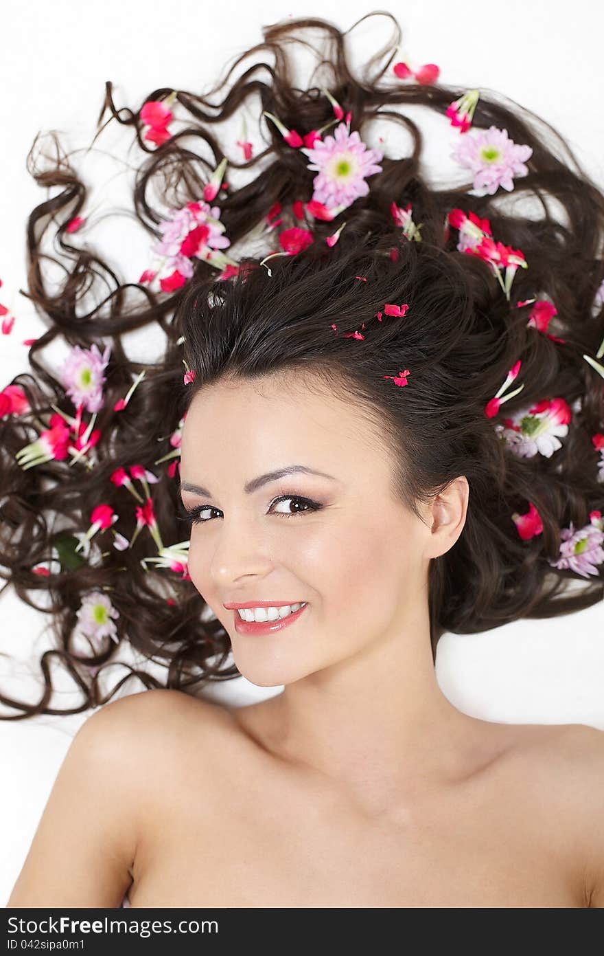 Pretty beautiful girl lying with bright red flowers in her hair bright makeup on white. Pretty beautiful girl lying with bright red flowers in her hair bright makeup on white