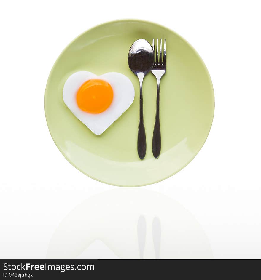 Fried egg heart and spoon on green dish