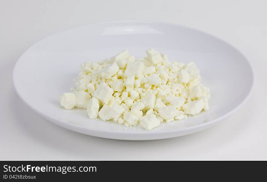 A small white plate of crumbled Feta cheese sitting on a white background.