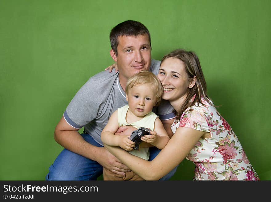 Young European family from three persons - mother, father and son. On a green background. Young European family from three persons - mother, father and son. On a green background.