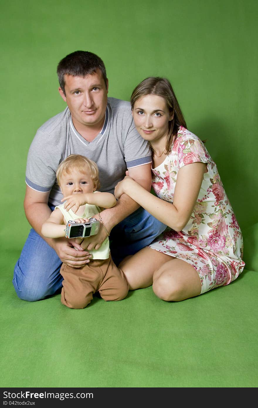 Young European family from three persons - mother, father and son. On a green background. Young European family from three persons - mother, father and son. On a green background.