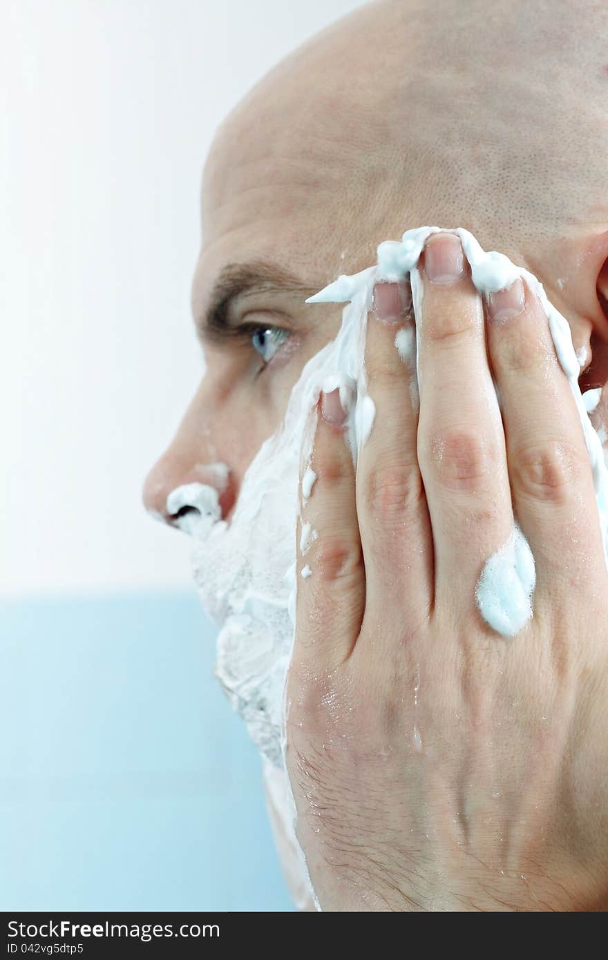 Young man applying shaving foam to face photographed in profile. Young man applying shaving foam to face photographed in profile