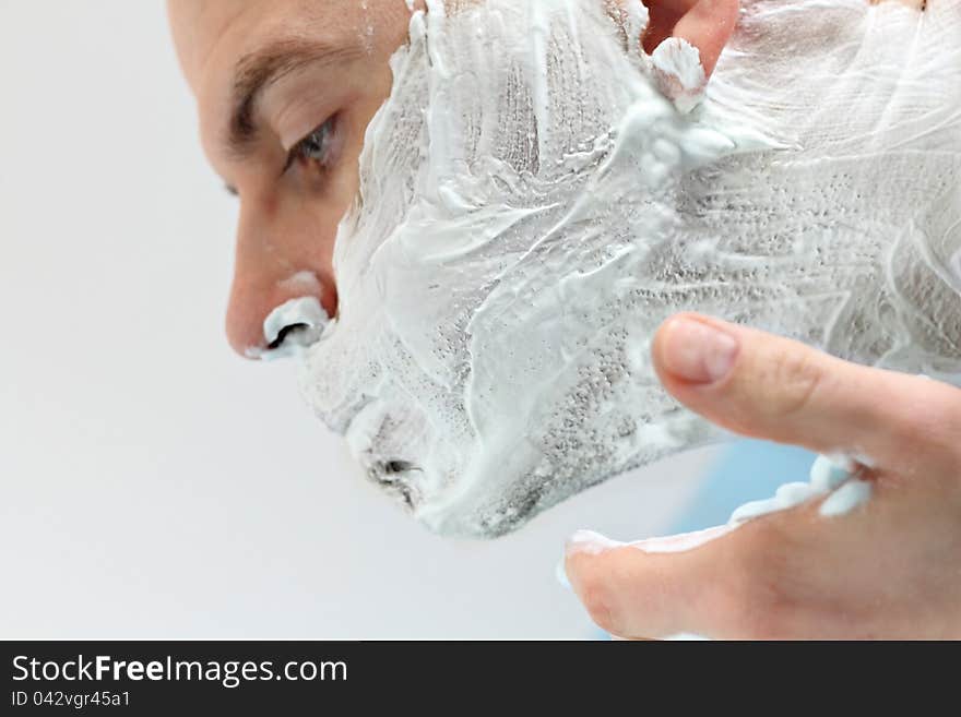 Young man applying shaving foam to face photographed in profile. Young man applying shaving foam to face photographed in profile