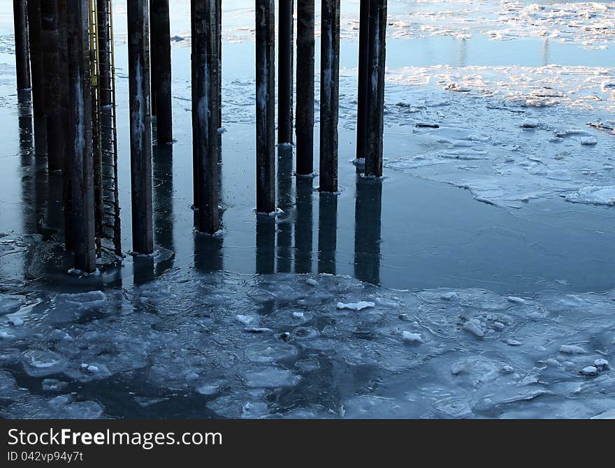 Old pier pillars in icy water of the harbor in winter.