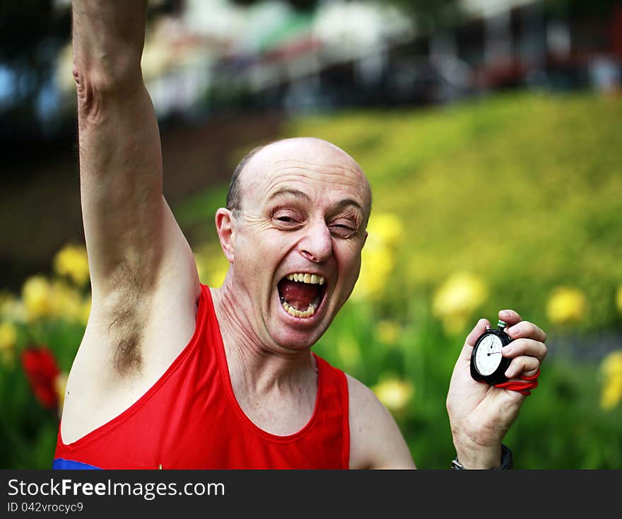 A close up of a businessman dressed in running attire, with a stopwatch in his hand elated that he has just broken his personal best time in a beautiful park. A close up of a businessman dressed in running attire, with a stopwatch in his hand elated that he has just broken his personal best time in a beautiful park.