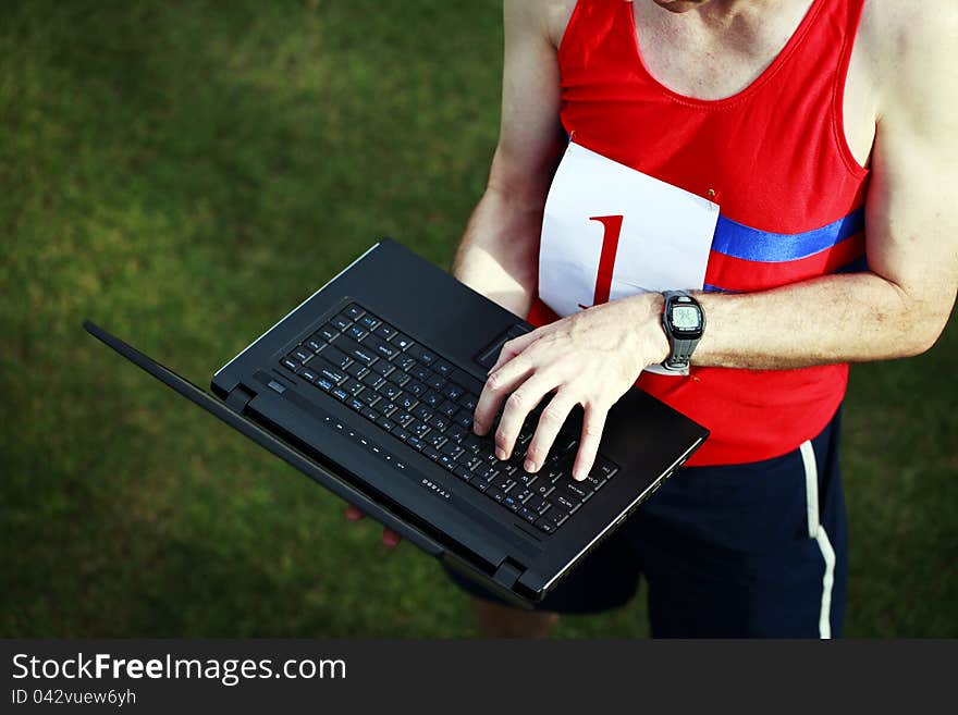 A close up of a businessman dressed in running attire with the number one on his chest, working on his laptop outside. A close up of a businessman dressed in running attire with the number one on his chest, working on his laptop outside.