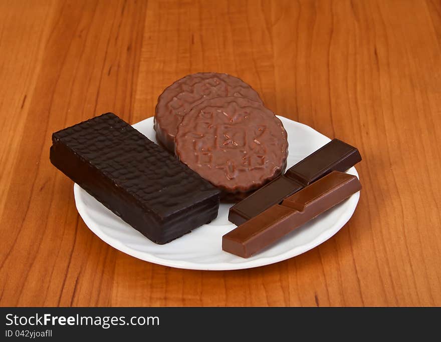 White saucer with chocolate candy on wooden table.