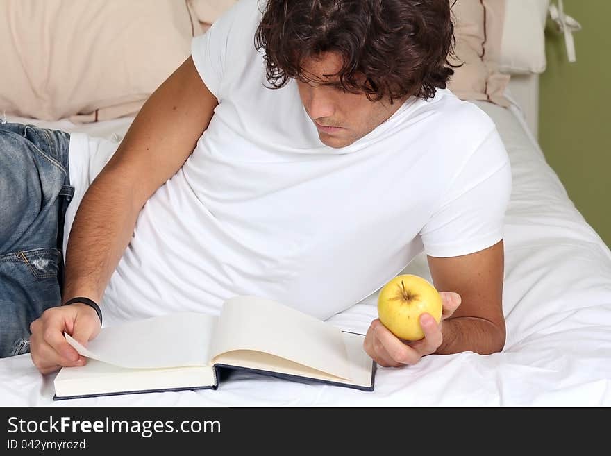 Young man focused on a book with an apple in hand. Young man focused on a book with an apple in hand