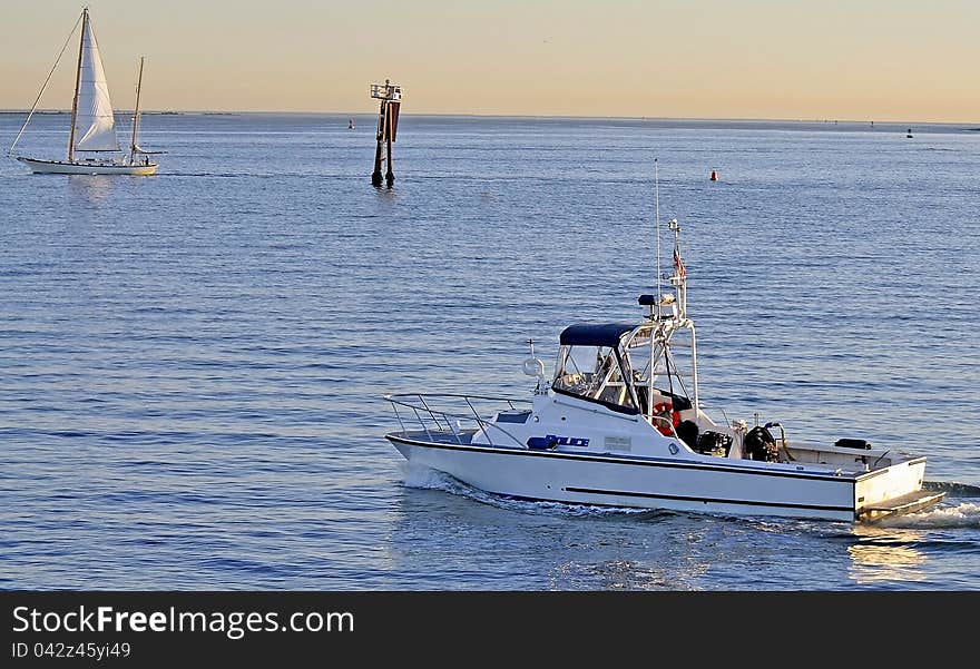 A Harbor Police Boat follows a Sailing Vessel into a Shipping Channel at Sunset. A Harbor Police Boat follows a Sailing Vessel into a Shipping Channel at Sunset.