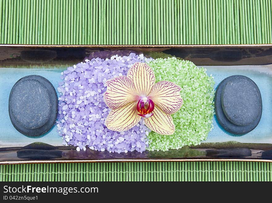 Spa concept with mineral bath salt, massage stones and orchid on green bamboo background