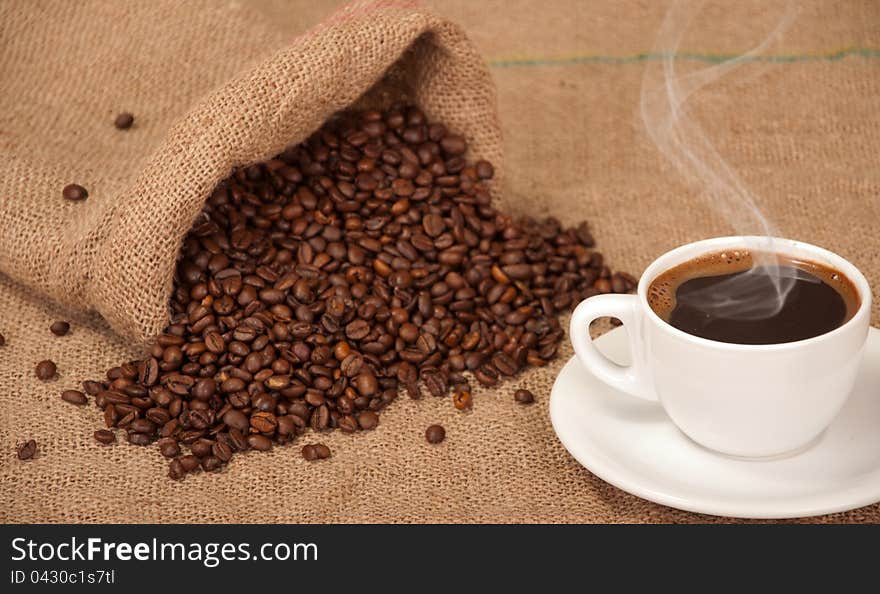 Cup with hot coffee and spilled coffee beans in addition to