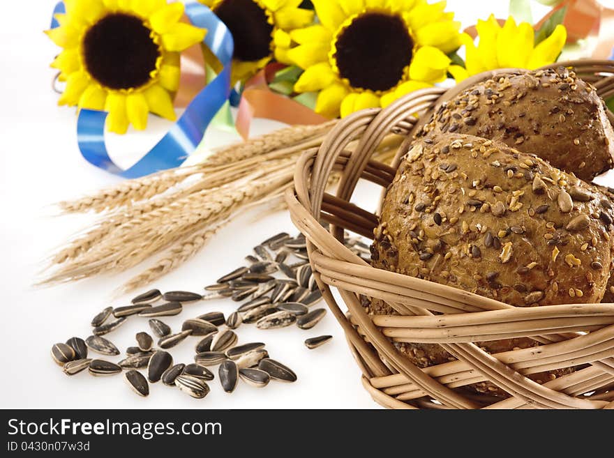 Whole-grain bread in a basked, sunflower seeds, wheat ears, sunflowers  and colored ribbons on a white background.