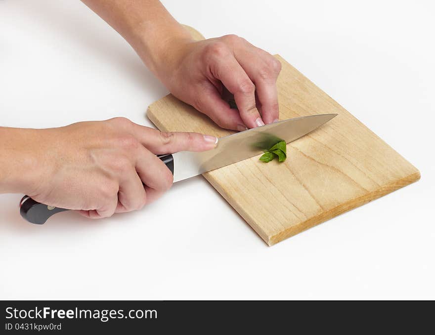 Using kitchen knife to cut rolled-up basil leaf on wooden chopping bard, close-up