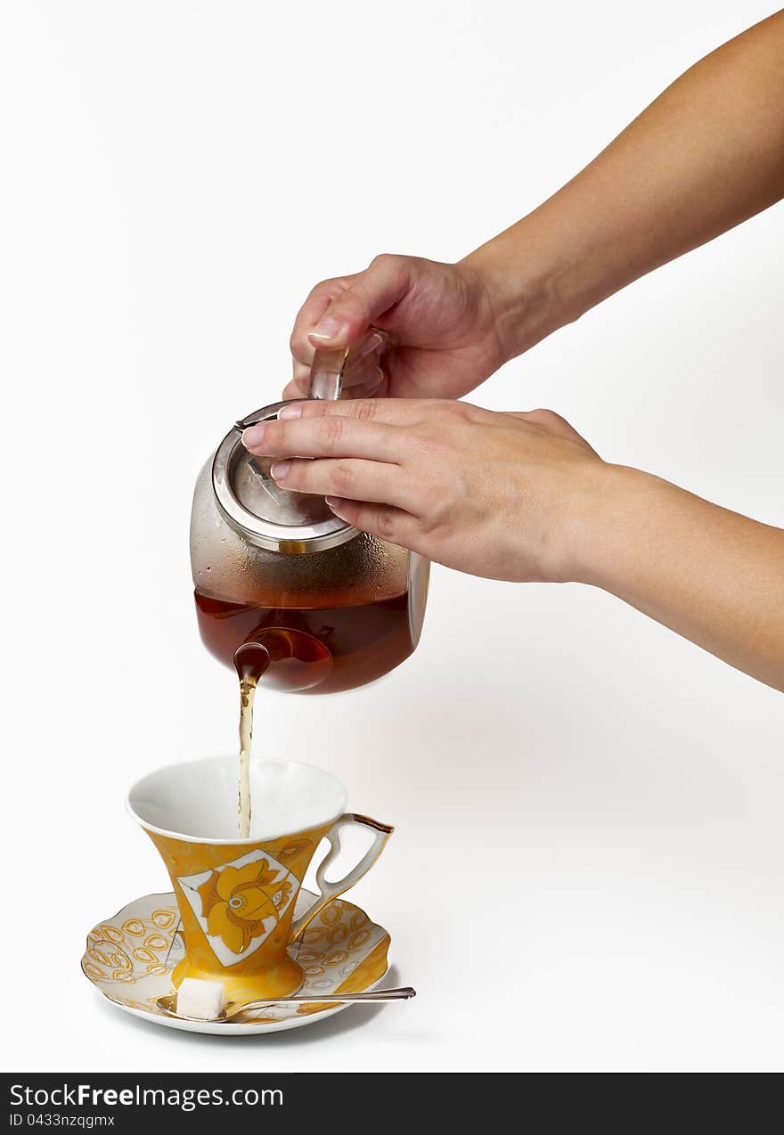 Tea being poured into glass tea cup on a white background.