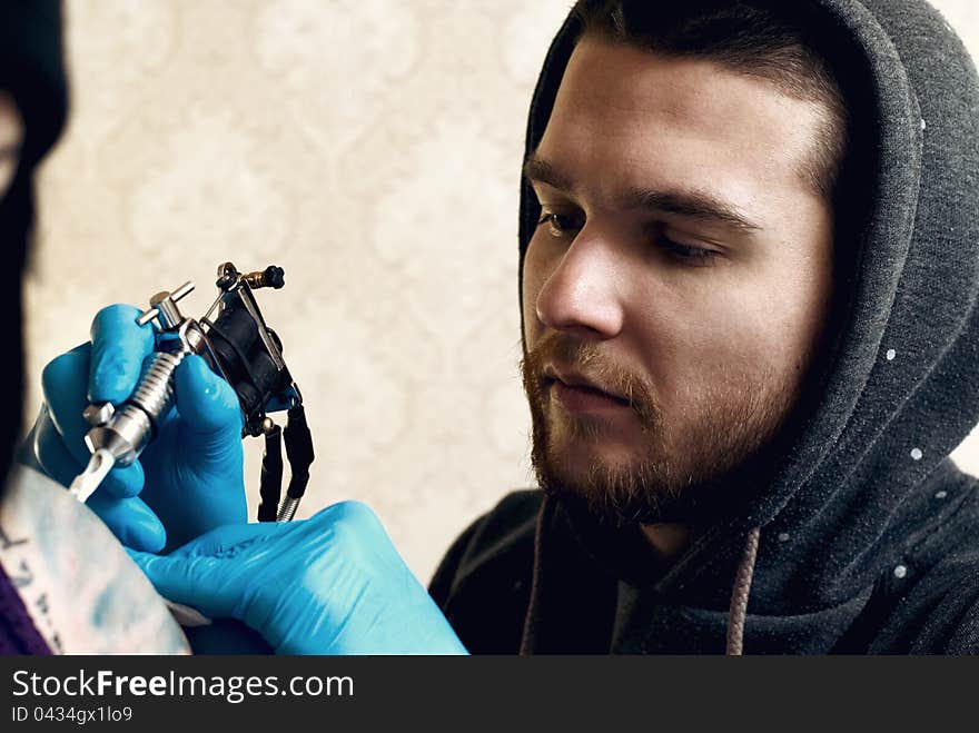 Bearded Caucasian tattooist creates a tattoo on a woman's shoulder, close up