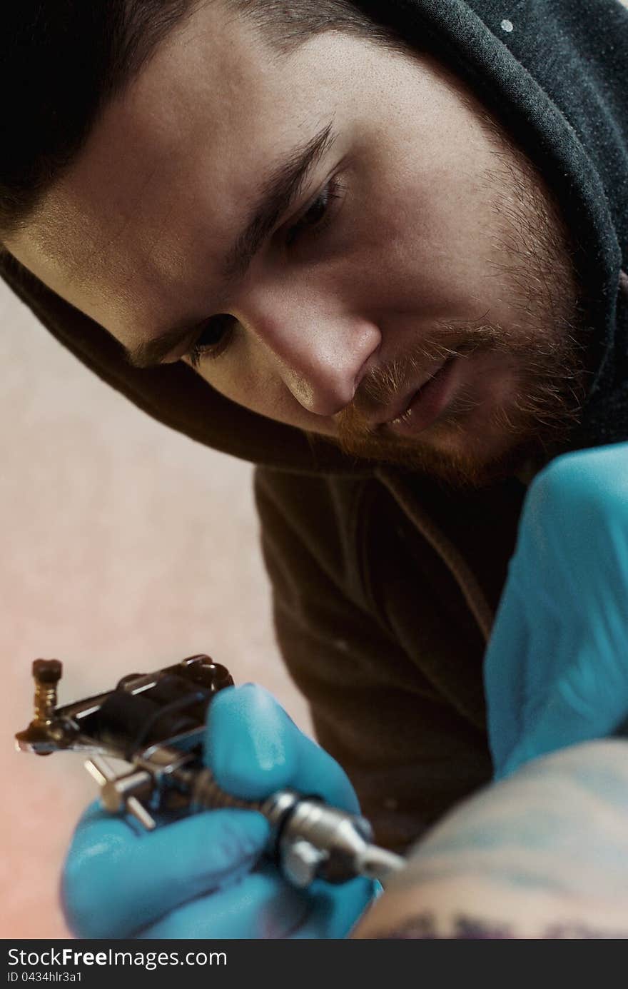 Bearded Caucasian tattooist creates a tattoo on a woman's shoulder, close up