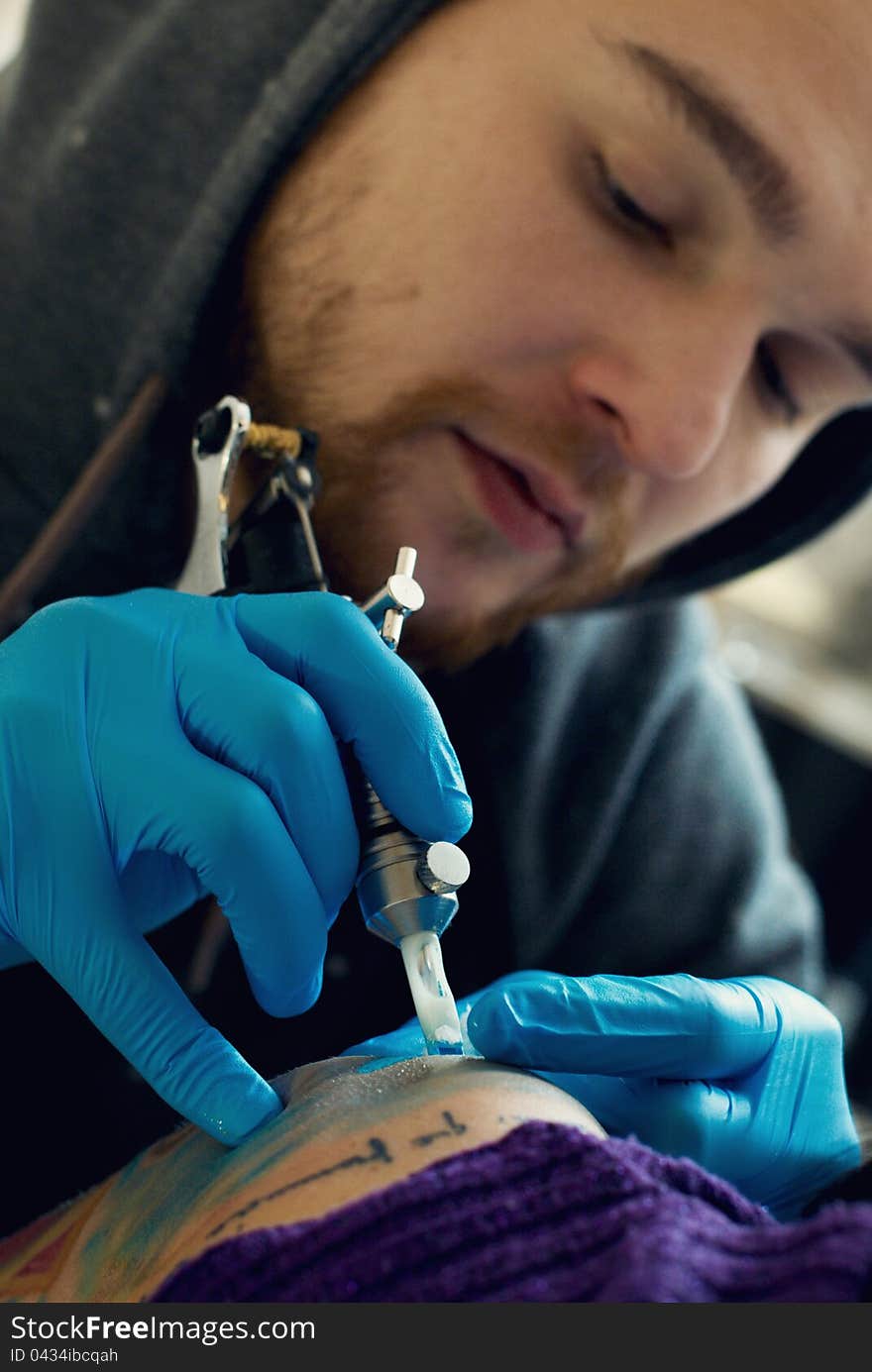 Bearded Caucasian tattooist creates a tattoo on a woman's shoulder, close up