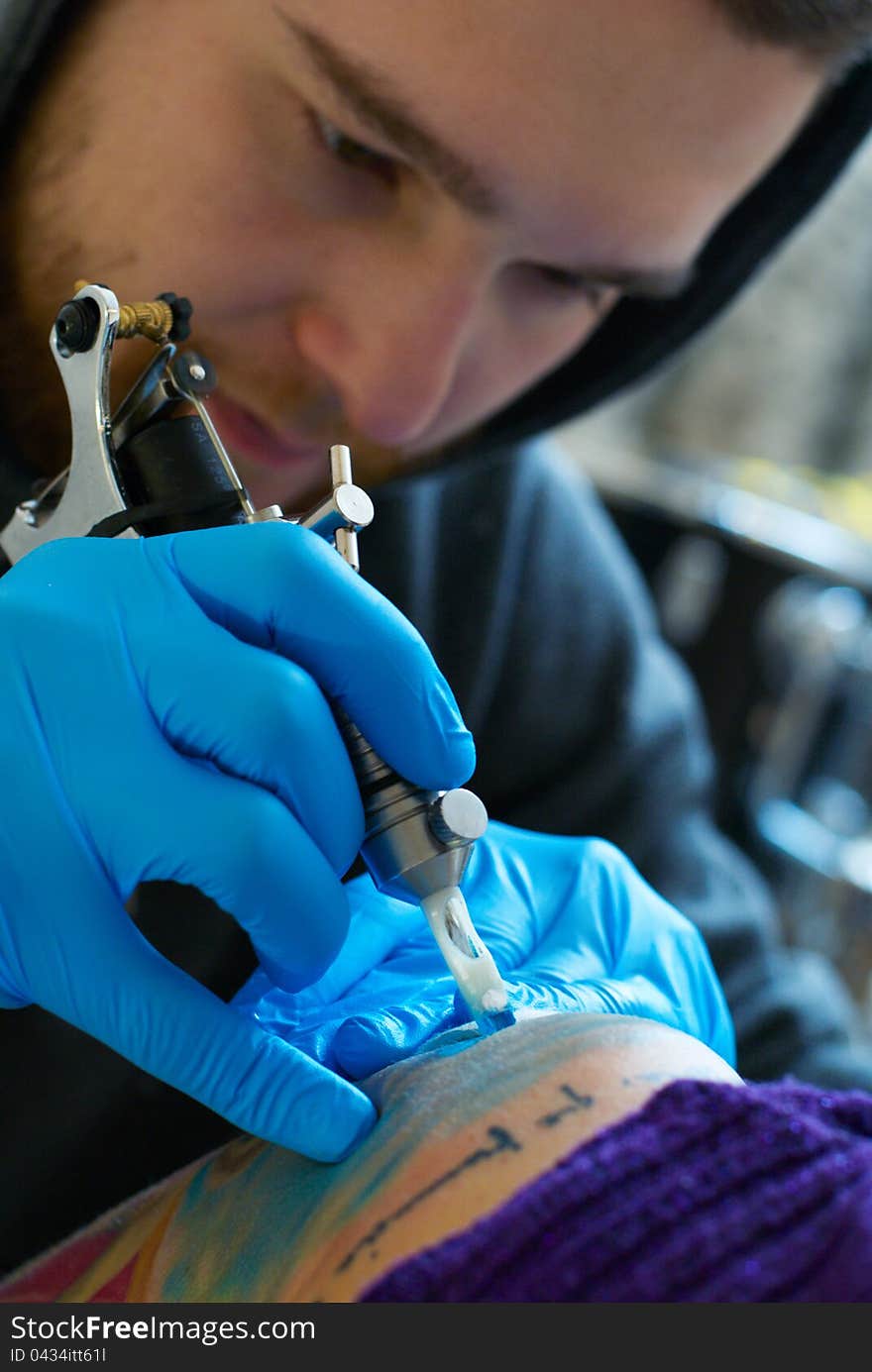 Bearded Caucasian tattooist creates a tattoo on a woman's shoulder, close up