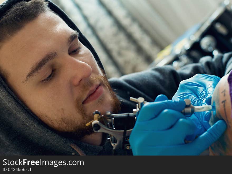 Bearded Caucasian tattooist creates a tattoo on a woman's shoulder, close up