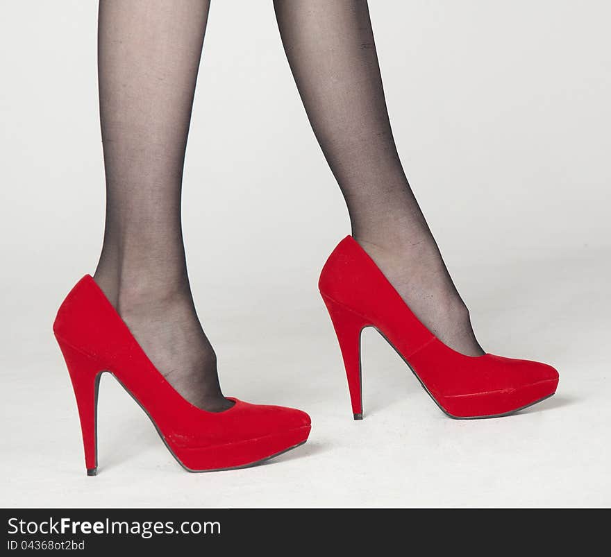 Close Up of Woman's Legs in Red Velvet High Heels and Dark Pantyhose Standing Against a White Background