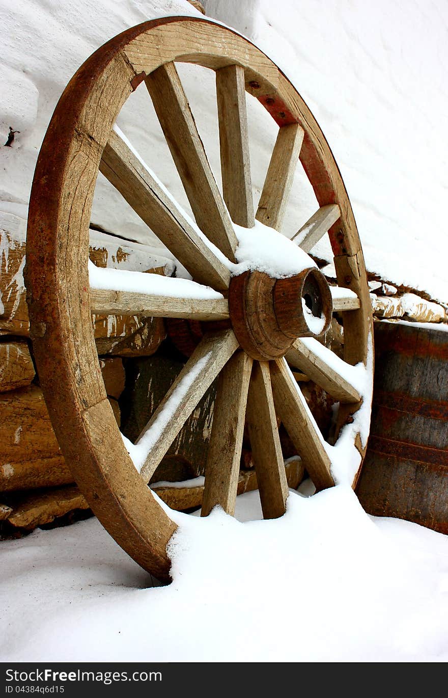 Antique wagon wheels in snow on a white brick wall with stones