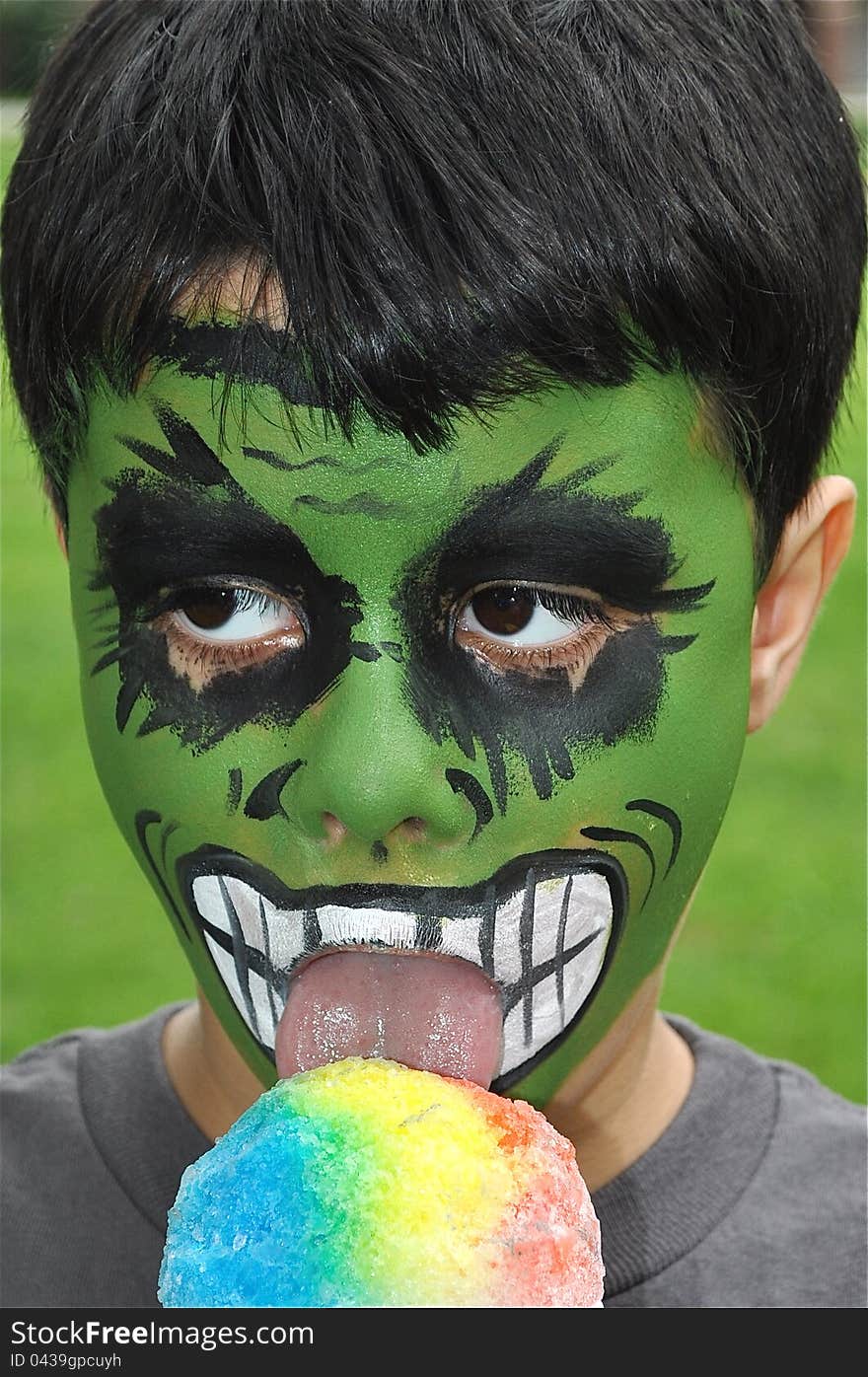 A little boy with his face painted is eating a delicious ice cream during a holiday. A little boy with his face painted is eating a delicious ice cream during a holiday