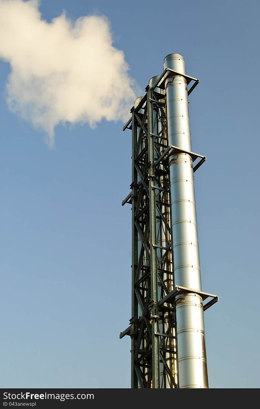 Vertical shot of industrial chimney with grey smoke on blue sky. Vertical shot of industrial chimney with grey smoke on blue sky.