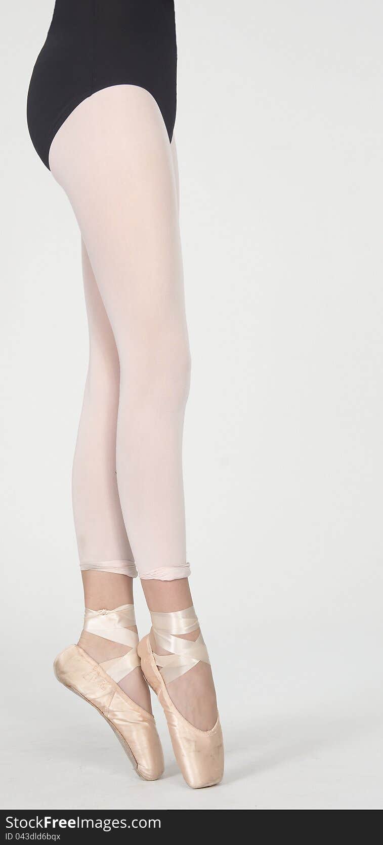 Close Up of Ballerina's Legs on Pointe in White Tights and Gold Pointe Shoes Wearing a Black Leotard Isolated Against a White Background. Close Up of Ballerina's Legs on Pointe in White Tights and Gold Pointe Shoes Wearing a Black Leotard Isolated Against a White Background