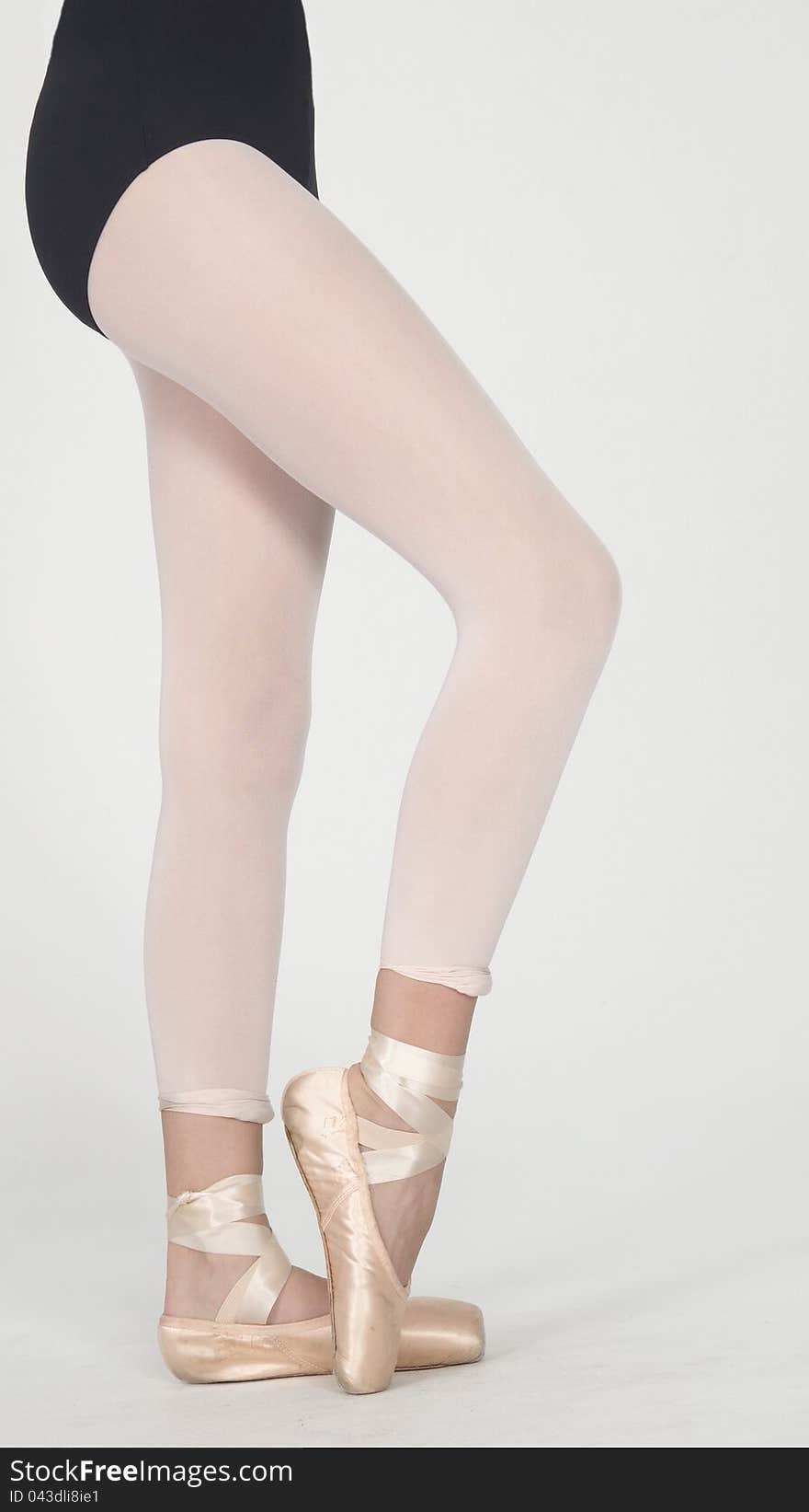 Close Up of Ballerina's Legs on Pointe in White Tights and Gold Pointe Shoes Wearing a Black Leotard Isolated Against a White Background. Close Up of Ballerina's Legs on Pointe in White Tights and Gold Pointe Shoes Wearing a Black Leotard Isolated Against a White Background