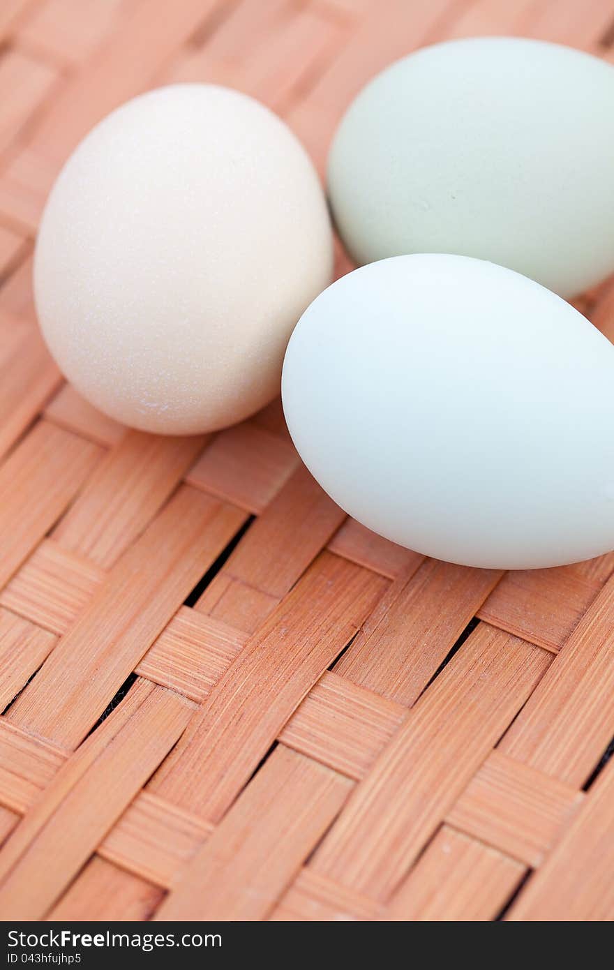 Close shot of three colorful organic eggs sitting in a cluster on a basket.