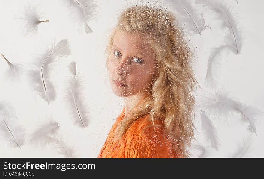 A unique portrait of a pretty teenage girl behind a clear, wet surface, surrounded by white feathers. A unique portrait of a pretty teenage girl behind a clear, wet surface, surrounded by white feathers